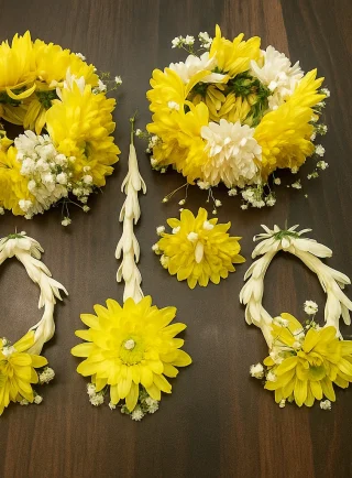 Complete yellow fresh flower jewellery set displayed on a wooden surface, including two full floral crowns, matching gajra-style necklaces, a long hair tika and centre piece, made with yellow and white blooms and baby’s breath by Lahore Blooms in Lahore.