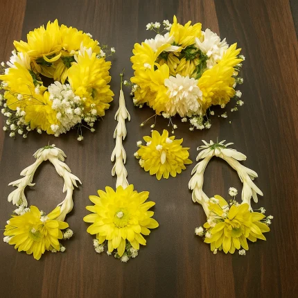 Complete yellow fresh flower jewellery set displayed on a wooden surface, including two full floral crowns, matching gajra-style necklaces, a long hair tika and centre piece, made with yellow and white blooms and baby’s breath by Lahore Blooms in Lahore.