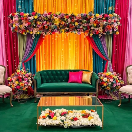 Premium mehndi stage decoration in Lahore with colorful drapes and floral backdrop sofa setup