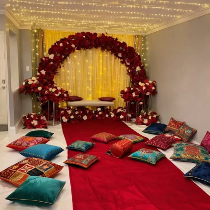 Royal indoor mehndi decoration setup in Lahore with red floral arch stage and floor seating