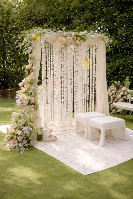 Outdoor nikah stage setup with white canopy frame, hanging floral strings and side flower arrangement in Lahore