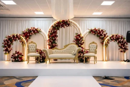 Wedding stage decoration in Lahore with golden arches, red floral arrangements and classic sofa seating
