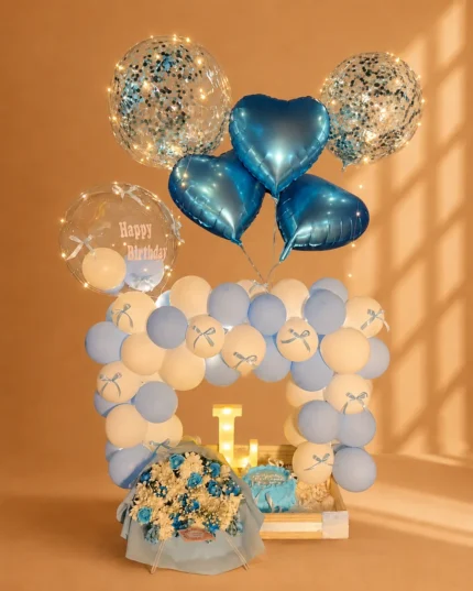 Blue and white birthday balloon arrangement with heart balloons, confetti balloons, blue cake, flower bouquet and illuminated letter in a wooden tray