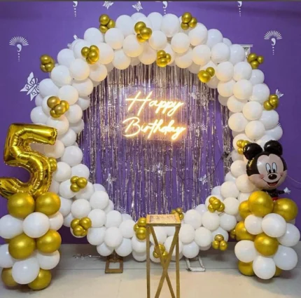 White and gold kids birthday decoration with balloon arch, customized age number, cartoon character balloon and Happy Birthday neon sign in Lahore