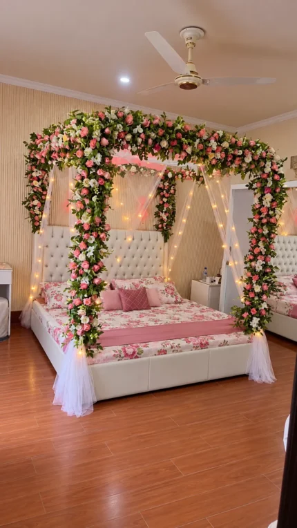 Fresh pink-and-white flowers across the canopy frame, with pale draping around the bed in a Lahore bridal bedroom