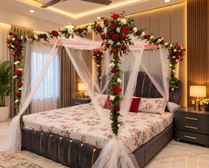 A balanced red-and-white floral frame overhead, sheer white corner drapes and a matching bed-side floral detail in a Lahore bridal bedroom