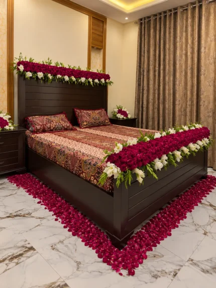 A low floral border tracing the bed, with red-and-white flowers concentrated around the headboard and foot rather than a full overhead canopy in a Lahore bridal bedroom