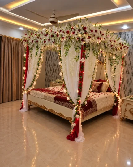 Fresh white flowers with red rose accents along the overhead canopy and corner posts in a Lahore bridal bedroom