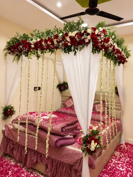 Fresh red-and-white canopy flowers with long hanging white flower strings around the bed in a Lahore bridal bedroom