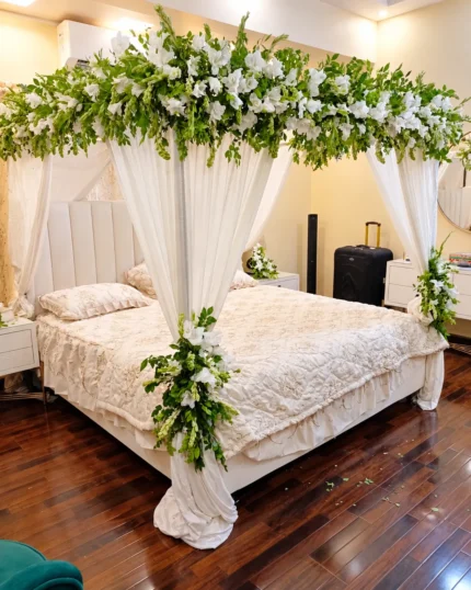 Fresh white flowers and green foliage over the bed, with white draping for a restrained all-white look in a Lahore bridal bedroom