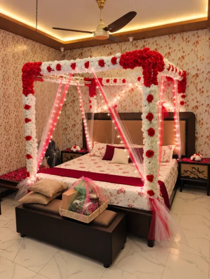 Artificial floral canopy in red and white, finished with warm fairy lights around the draped bed in a Lahore bridal bedroom