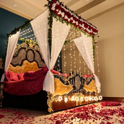 Fresh red-and-white flowers on the canopy frame with warm lights and white net drapes in a Lahore bridal bedroom