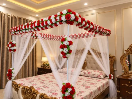 A structured red-and-white artificial floral canopy with sheer white drapes around the bed in a Lahore bridal bedroom