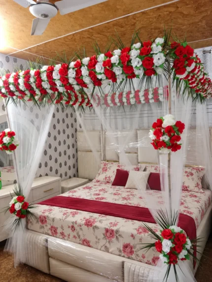 Artificial red-and-white canopy flowers, with a small accent of fresh palm leaves at the base in a Lahore bridal bedroom