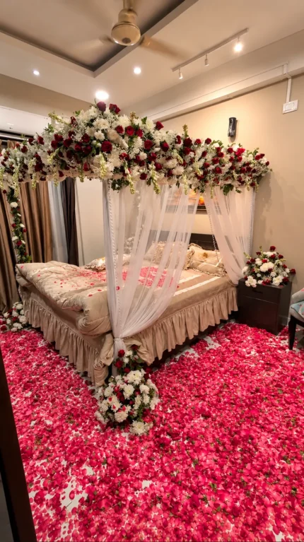 A large fresh red-and-white flower canopy with dense overhead coverage and floral strands around the bed in a Lahore bridal bedroom