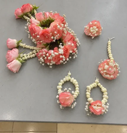 Coral pink roses, white buds and filler flowers with pearl-style details and hanging rose accents.