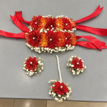 Orange-red blooms and white filler flowers, wide ribbon-tied wrist pieces, earrings and forehead ornament.