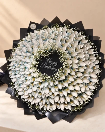 A large circular arrangement of rolled notes with white filler flowers and a central message area.