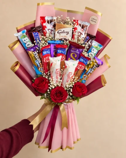 A tall mixed chocolate bar arrangement with red roses in pink and gold wrapping.