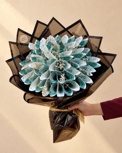 Folded notes arranged as a flower-like bloom with white filler flowers in black and gold wrapping.
