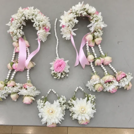 White flowers and pink rose accents with pearl-style strands, coordinated floral crown, wrist pieces, earrings and forehead ornament.