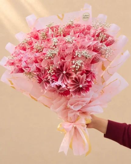Pink folded banknote blooms with baby's breath in pink wrapping.
