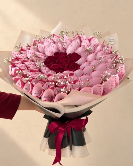 Pink folded notes surrounding a deep red rose centre in pale pink wrapping.