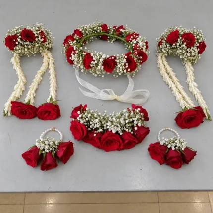 Red roses and white filler flowers coordinated across a floral crown and matching jewellery, with hanging floral strands.