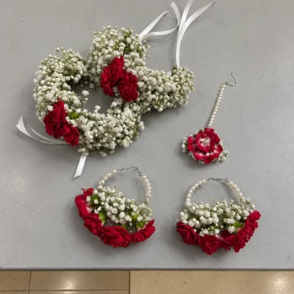 Red roses surrounded by small white filler flowers, matching wrist pieces, earrings and forehead ornament.